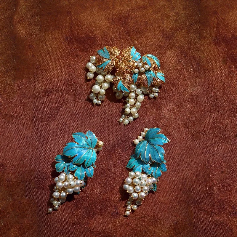 Close up of the blue enamel grape design with a faux pearl accent, showing gold tone metal detail on a deep brown background
