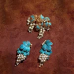Pair of blue enamel grape earrings with faux pearl drops shown from two angles on a deep red background