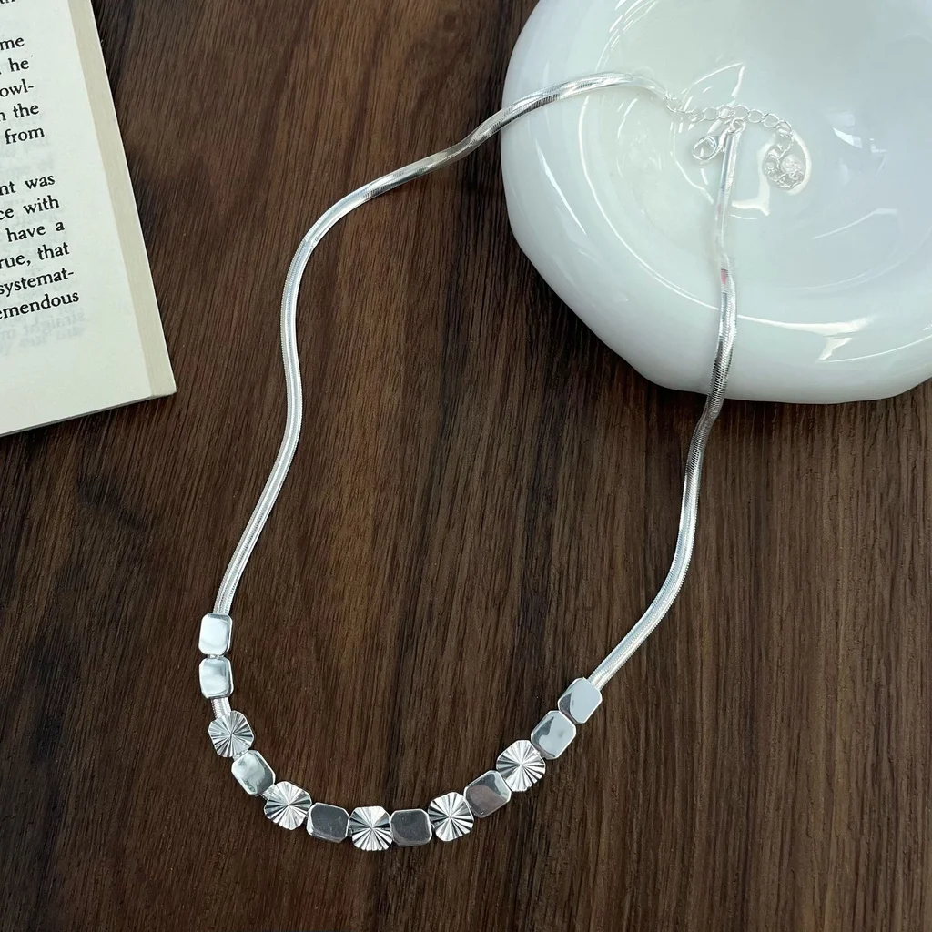 Faceted cube sterling silver snake‑chain choker flat lay shot on dark wooden surface