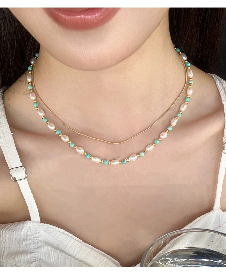 Woman wearing freshwater pearl turquoise collarbone necklace layered with thin gold snake chain