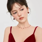 Model in red velvet dress wearing matching red agate necklace and earring set, french vintage women jewelry