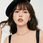 Stylish woman with beret wearing french vintage red agate station necklace and matching earrings, dainty gold‑tone jewelry set