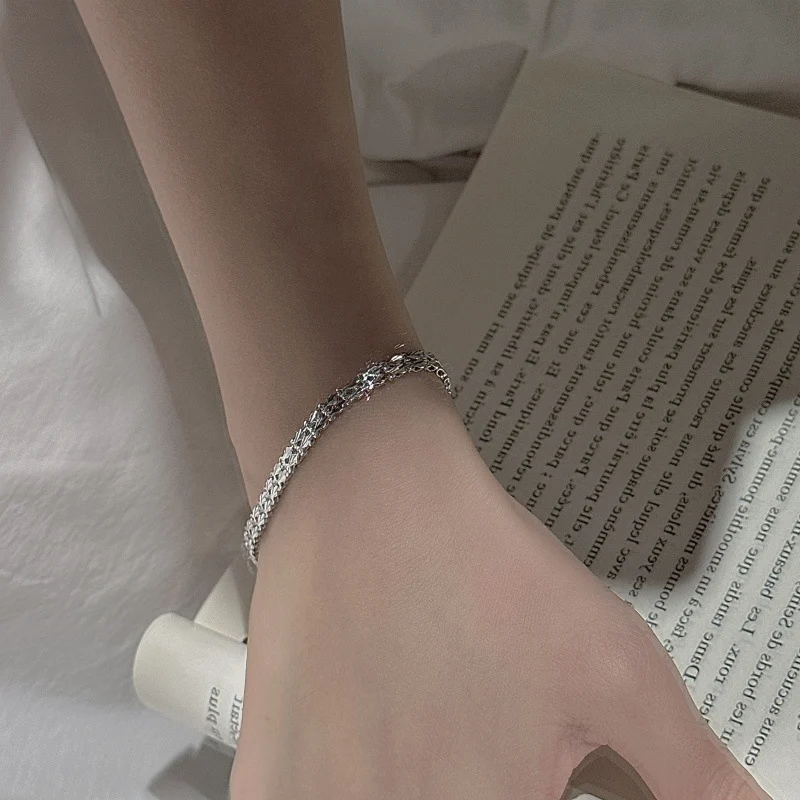 Gold tone S999 shell textured woven chain bracelet laid flat on white ceramic shell dish, showing hook clasp and heart extender chain, women stacking jewelry
