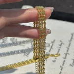 Hand holding gold‑toned S999 fine silver three‑row rhombus woven bracelet, close‑up view of woven chain texture