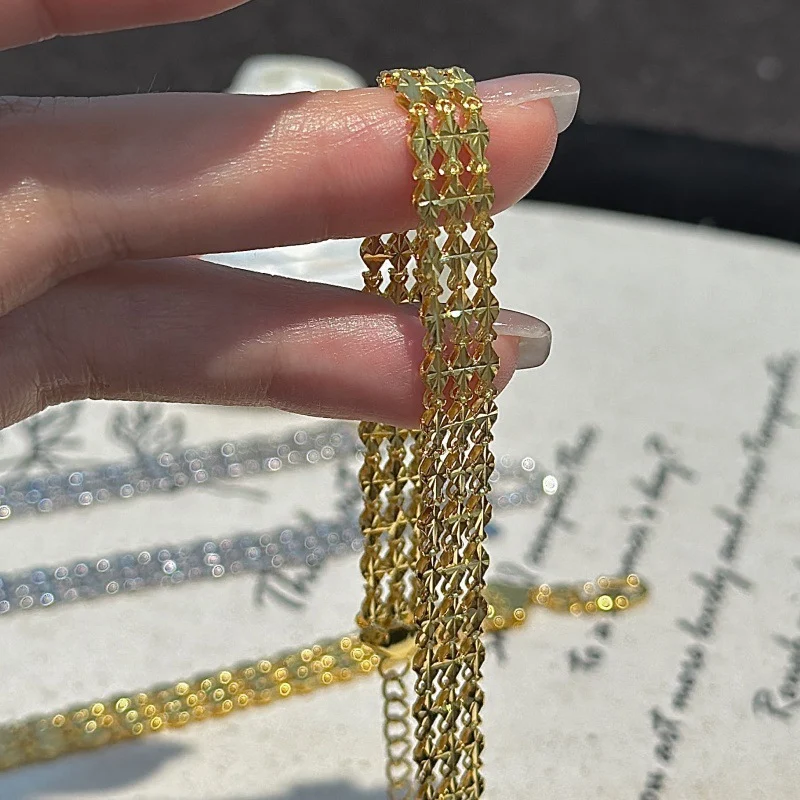 Hand holding gold‑toned S999 fine silver three‑row rhombus woven bracelet, close‑up view of woven chain texture