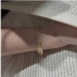 Gold‑toned S999 fine silver three‑row rhombus woven bracelet worn on female wrist beside open vintage book, medieval vintage dainty women jewelry