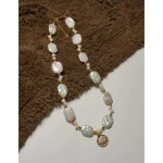 Baroque freshwater pearl choker laid flat on soft brown fabric, featuring zircon eye pendant