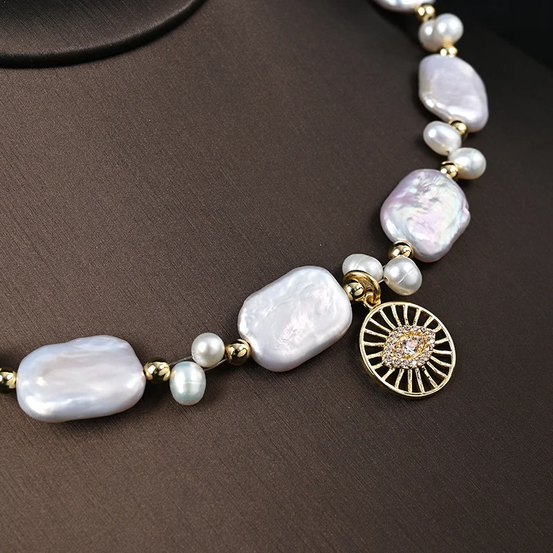 Close-up macro shot of sun-shaped zircon pendant and irregular baroque freshwater pearls on gold necklace
