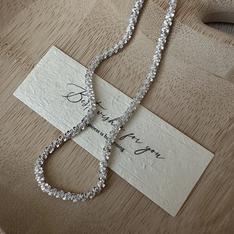 Close-up flat lay of S925 sterling silver crushed sparkle bead chain detail, shimmering silver fragments texture