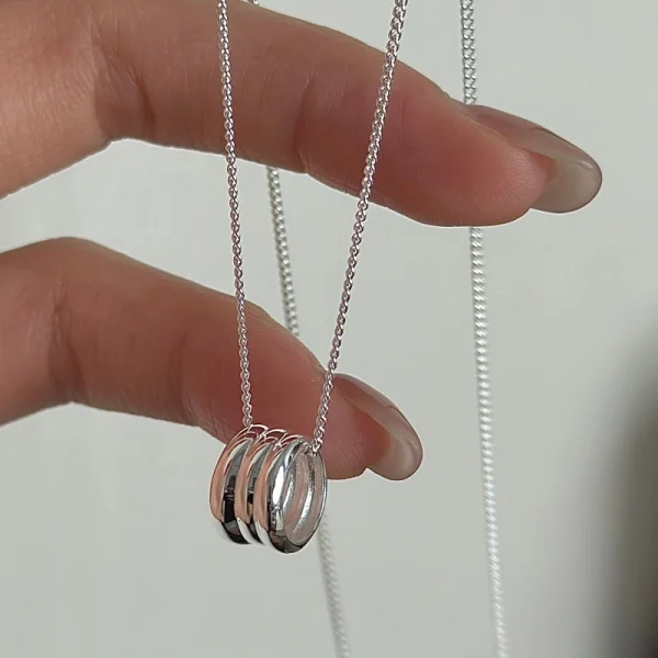 S925 sterling silver multi stacked ring pendant necklace held in hand, polished glossy silver circle pendant with fine chain, minimalist jewelry product shot