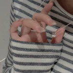 Hand holding S925 sterling silver multi stacked ring pendant necklace, collarbone wearing demonstration with striped sweater