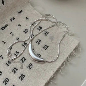 S925 sterling silver matte curved crescent pendant snake chain necklace laid on linen calendar fabric