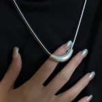 Close up of matte curved crescent S925 silver necklace held by hand with glossy manicure