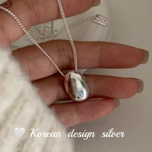 S925 sterling silver oval bean pendant necklace held in hand with cream knit sleeve, Korean minimalist design