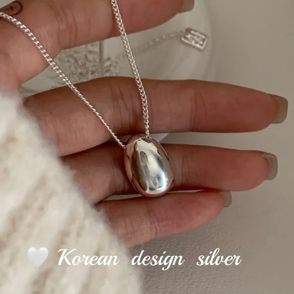 S925 sterling silver oval bean pendant necklace held in hand with cream knit sleeve, Korean minimalist design