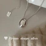 S925 sterling silver oval bean pendant necklace flat lay with cream knit fabric and white ceramic dish