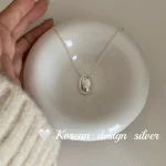 S925 sterling silver oval pebble pendant necklace on white ceramic bowl with cream knit sleeve