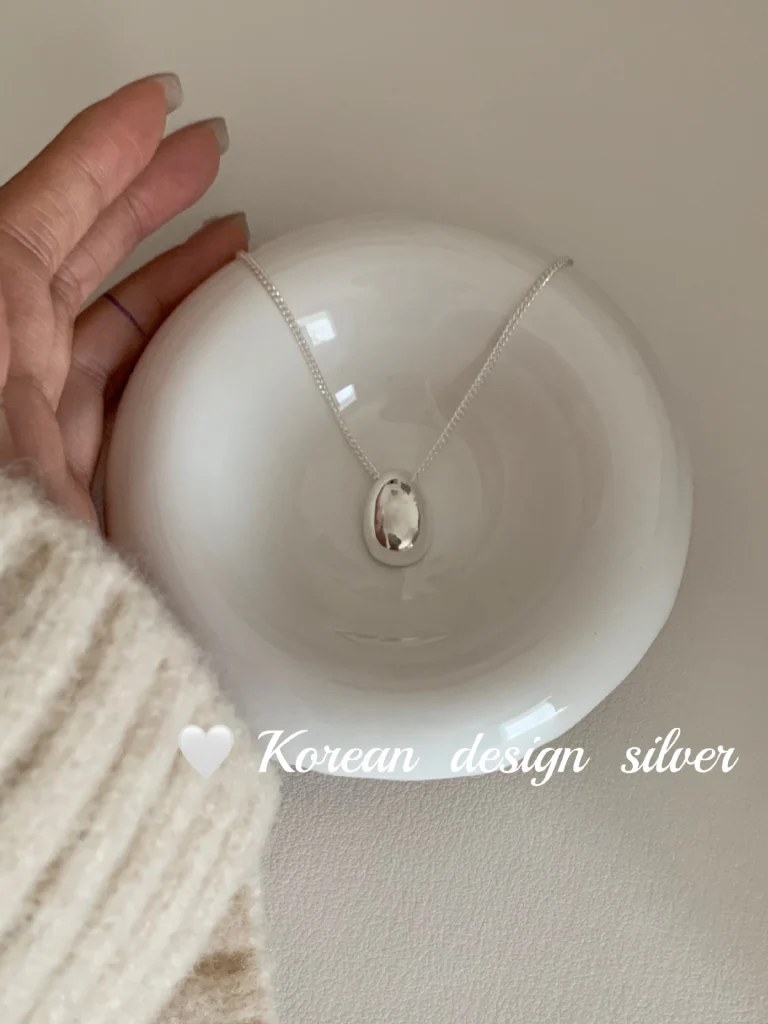 S925 sterling silver oval pebble pendant necklace on white ceramic bowl with cream knit sleeve