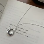 S925 silver hollow circle donut necklace flat lay on open book, aesthetic product photo
