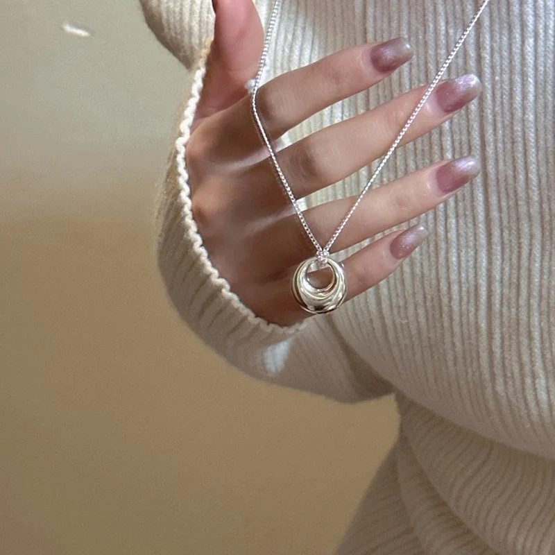 Close-up of S925 silver hollow donut necklace worn on neck, hand holding pendant, knit sweater styling
