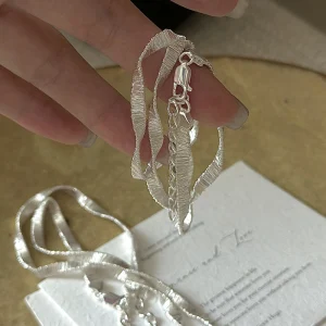 S925 sterling silver wavy ribbon flat chain necklace held on white card, main product photo