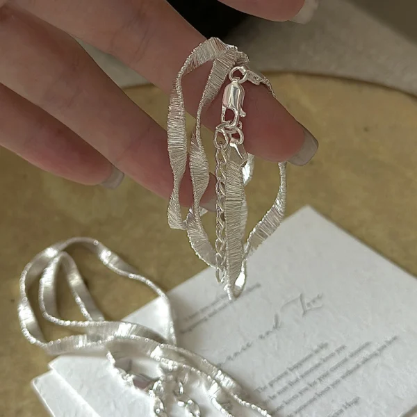 S925 sterling silver wavy ribbon flat chain necklace held on white card, main product photo
