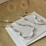 S925 sterling silver wavy ribbon flat chain necklace laid flat on vintage paper card, product detail flat lay