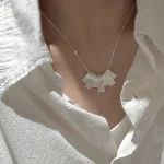 Side view of S925 sterling silver brushed fan necklace worn with loose white shirt, natural sunlight, quiet luxury style