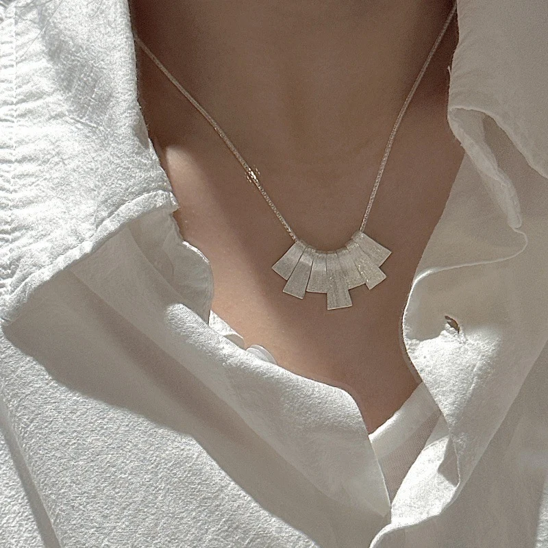 Side view of S925 sterling silver brushed fan necklace worn with loose white shirt, natural sunlight, quiet luxury style