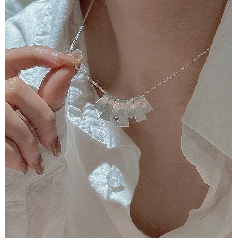 Hand holding S925 brushed fan silver necklace, collarbone wearing preview with white shirt