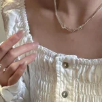 S925 sterling silver snake necklace worn with white ruched blouse, hand with silver ring beside neckline