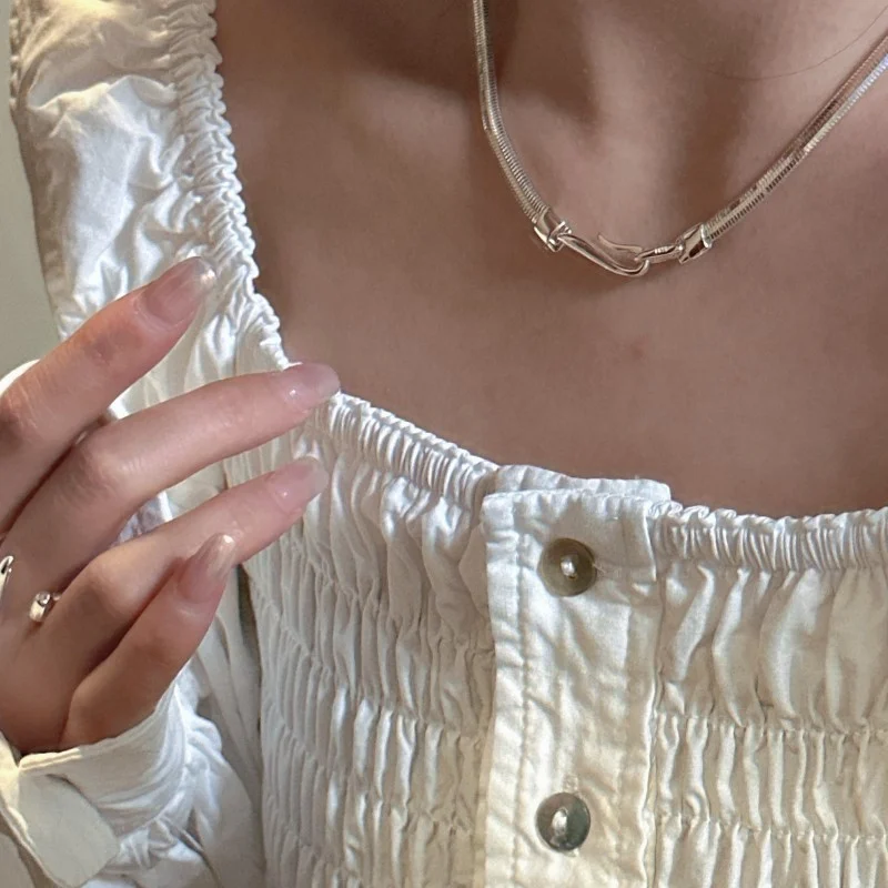 S925 sterling silver snake necklace worn with white ruched blouse, hand with silver ring beside neckline