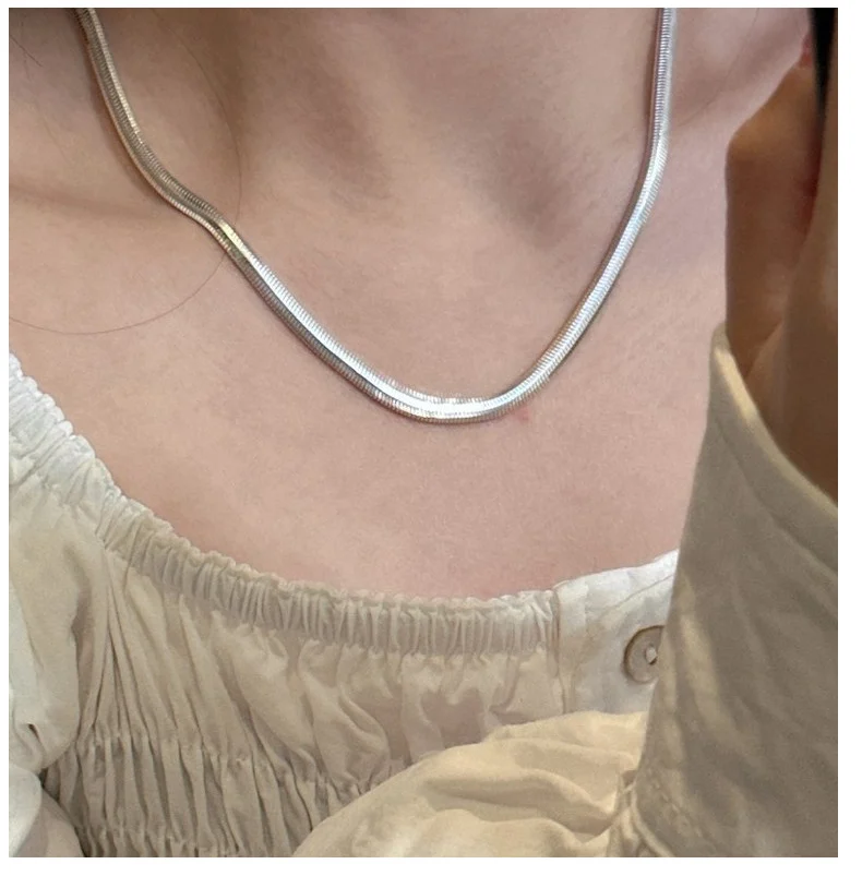 Close-up shot of S925 flat snake chain necklace resting on collarbone, white square neck top