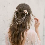 Model with wavy brown hair wearing gold floral pearl cascade double clip, half-up bridal hairstyle